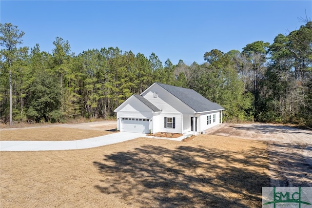 ranch-style house with driveway, a forest view, and an attached garage