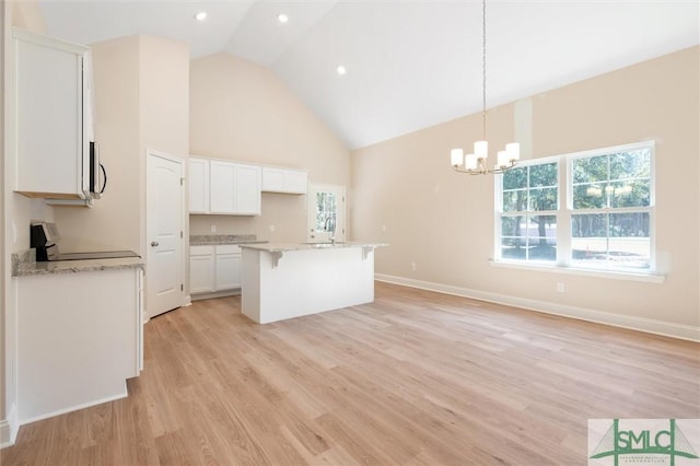 kitchen with high vaulted ceiling, light wood-style floors, white cabinets, range, and a kitchen bar