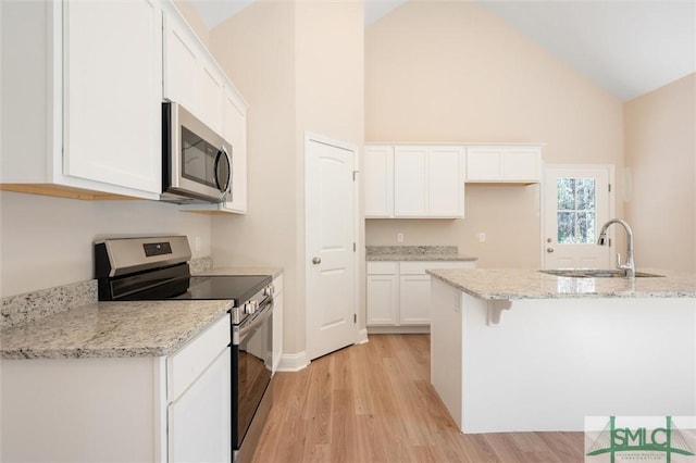 kitchen with a sink, white cabinets, appliances with stainless steel finishes, light wood-type flooring, and light stone countertops