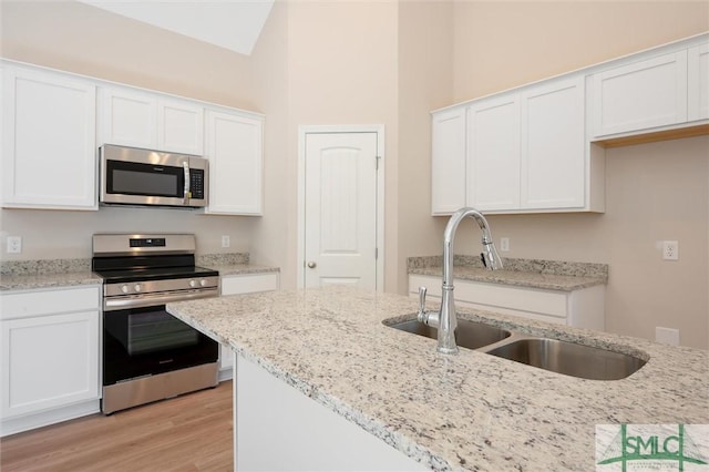 kitchen with a sink, white cabinetry, appliances with stainless steel finishes, light stone countertops, and light wood finished floors