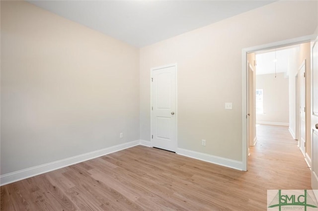 empty room with light wood-type flooring, attic access, and baseboards