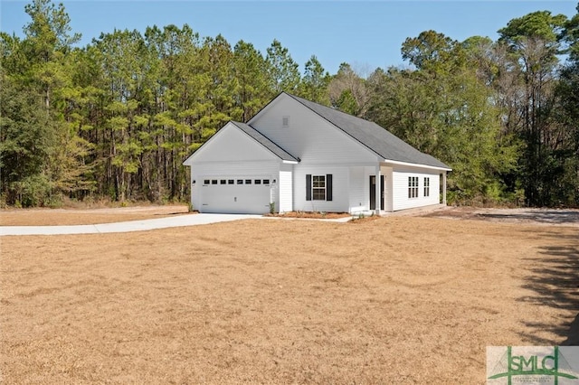 ranch-style home with a garage, concrete driveway, and a wooded view