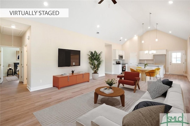 living area featuring high vaulted ceiling, light wood-type flooring, attic access, and a ceiling fan