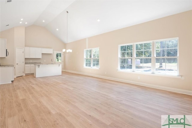 unfurnished living room featuring a chandelier, a wealth of natural light, high vaulted ceiling, and light wood finished floors