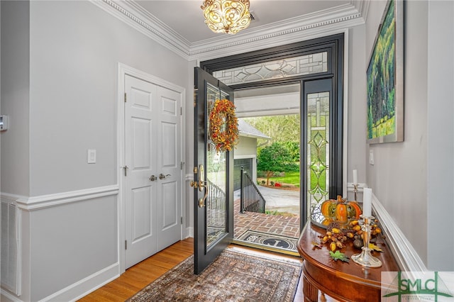 foyer featuring crown molding, wood-type flooring, and a notable chandelier