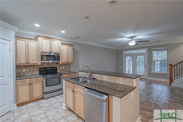 kitchen with sink, dark stone countertops, ornamental molding, stainless steel appliances, and a kitchen island with sink