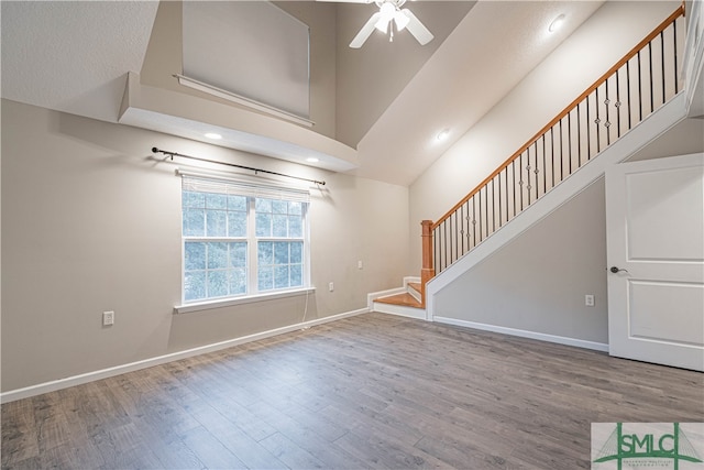 unfurnished living room featuring ceiling fan, wood-type flooring, and a towering ceiling