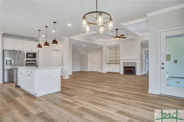 kitchen with hanging light fixtures, appliances with stainless steel finishes, white cabinetry, and a kitchen island with sink