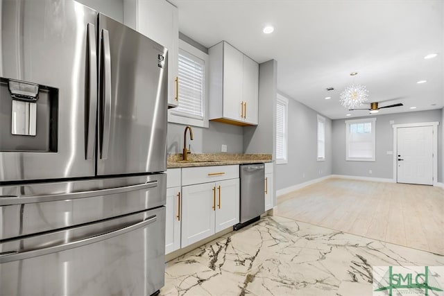 kitchen with light stone countertops, appliances with stainless steel finishes, white cabinetry, sink, and ceiling fan