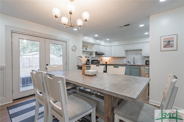 dining room with french doors, hardwood / wood-style floors, a textured ceiling, and an inviting chandelier