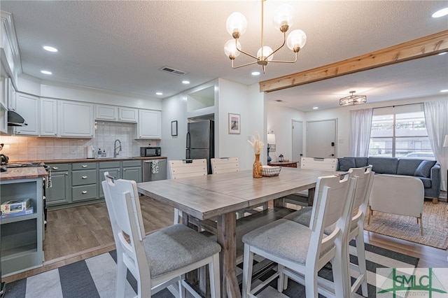 dining room with sink, light hardwood / wood-style floors, a textured ceiling, and a notable chandelier