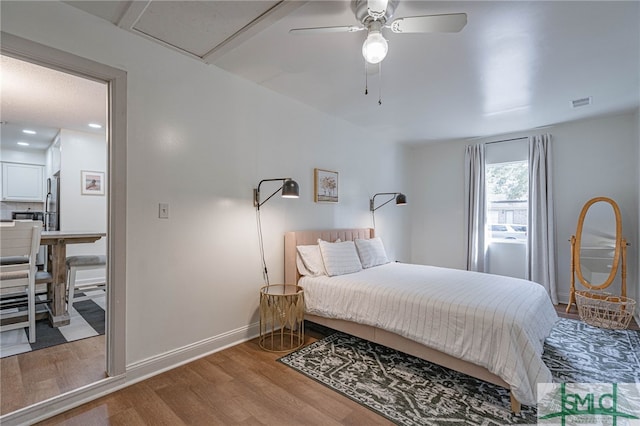 bedroom with hardwood / wood-style floors, ceiling fan, and stainless steel refrigerator