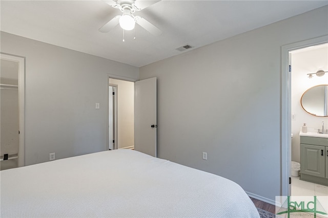 bedroom featuring light wood-type flooring, ensuite bath, ceiling fan, sink, and a closet