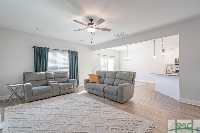 living room featuring ceiling fan, light hardwood / wood-style flooring, a textured ceiling, and sink