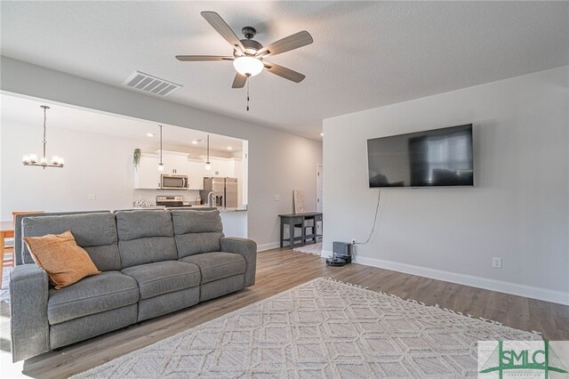 living room featuring ceiling fan with notable chandelier, light wood-type flooring, and a textured ceiling