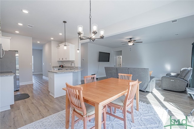 dining space with ceiling fan with notable chandelier, light hardwood / wood-style flooring, and sink