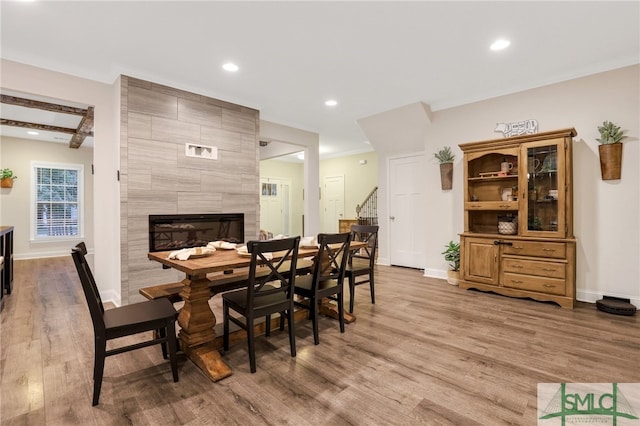 dining area with hardwood / wood-style floors, ornamental molding, beamed ceiling, and a tiled fireplace