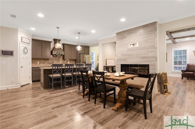 dining area with a fireplace, ornamental molding, light hardwood / wood-style floors, and beamed ceiling