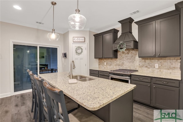 kitchen featuring pendant lighting, sink, an island with sink, stainless steel range oven, and custom range hood