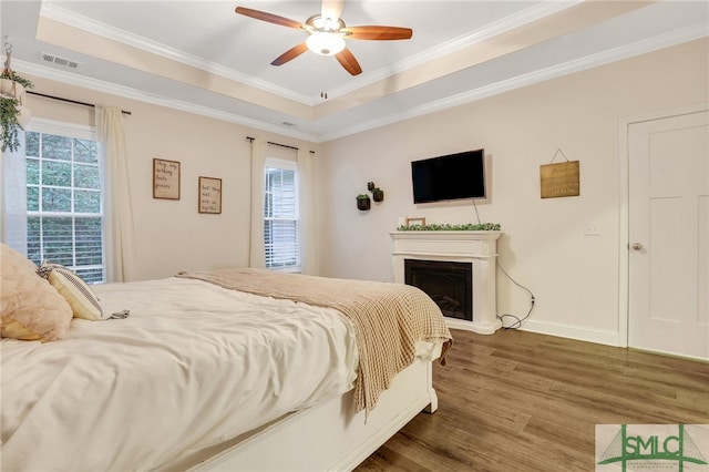 bedroom with ceiling fan, a raised ceiling, ornamental molding, and dark wood-type flooring