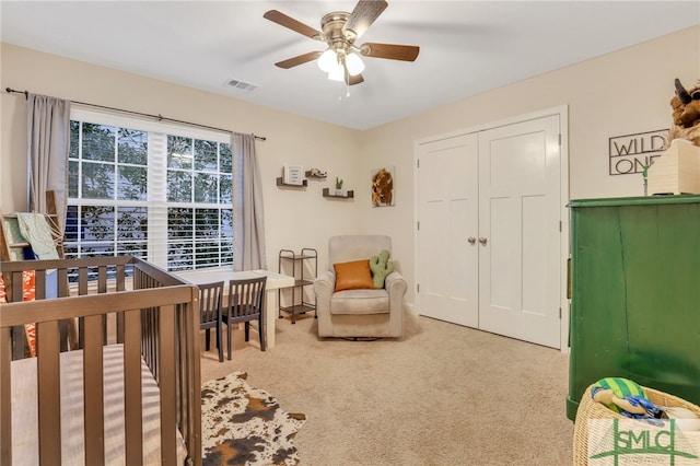 carpeted bedroom with ceiling fan, a closet, and a nursery area