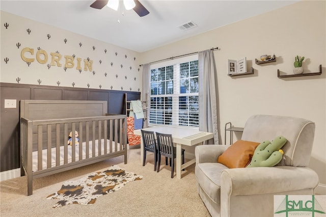 carpeted bedroom with ceiling fan and a crib