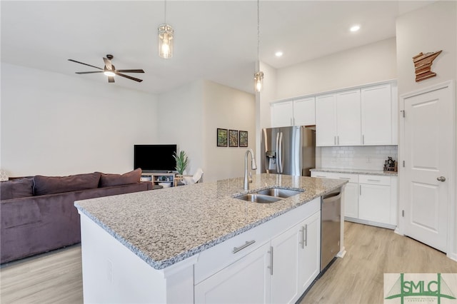 kitchen featuring stainless steel appliances, hanging light fixtures, light hardwood / wood-style flooring, a kitchen island with sink, and white cabinets