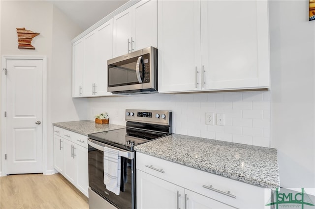 kitchen featuring light stone countertops, light wood-type flooring, tasteful backsplash, white cabinetry, and stainless steel appliances