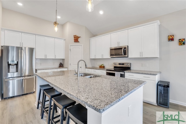 kitchen with appliances with stainless steel finishes, light stone counters, sink, a center island with sink, and white cabinets