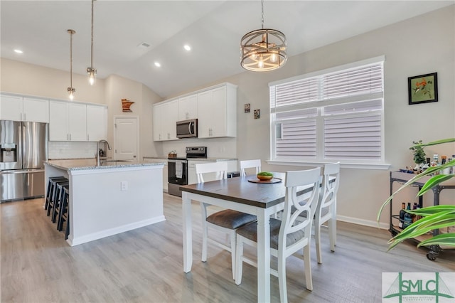 kitchen featuring white cabinetry, hanging light fixtures, stainless steel appliances, lofted ceiling, and a center island with sink