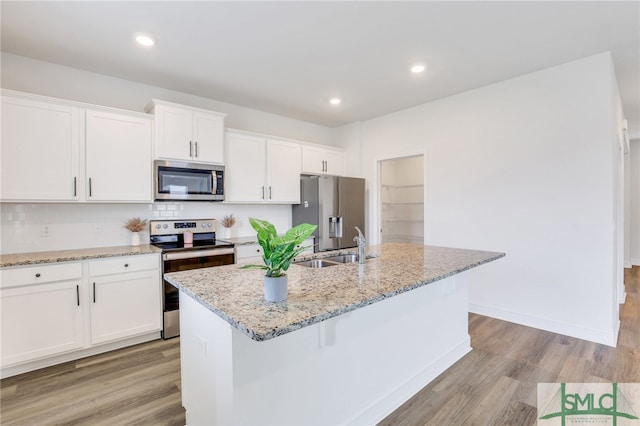 kitchen with light stone countertops, stainless steel appliances, a kitchen island with sink, white cabinets, and light hardwood / wood-style floors