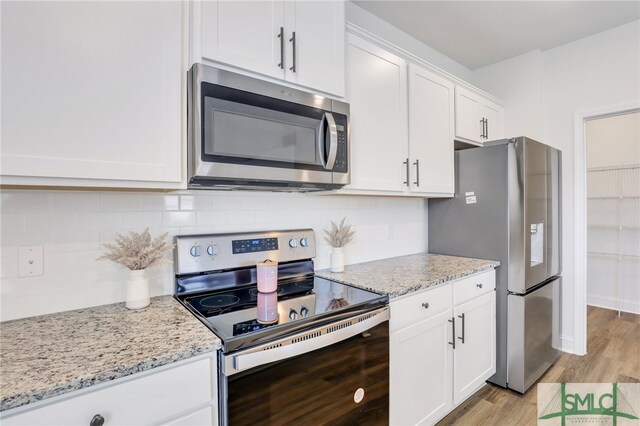 kitchen with white cabinets, light stone countertops, stainless steel appliances, and light hardwood / wood-style flooring