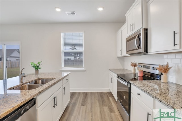 kitchen with white cabinetry, sink, stainless steel appliances, light stone counters, and light hardwood / wood-style flooring