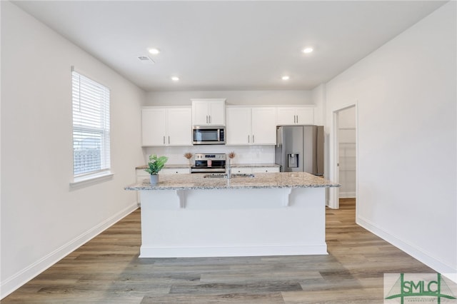 kitchen featuring a kitchen bar, light stone counters, stainless steel appliances, white cabinets, and an island with sink