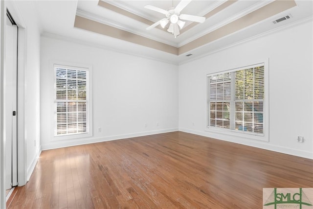 spare room with visible vents, ceiling fan, a tray ceiling, ornamental molding, and wood-type flooring