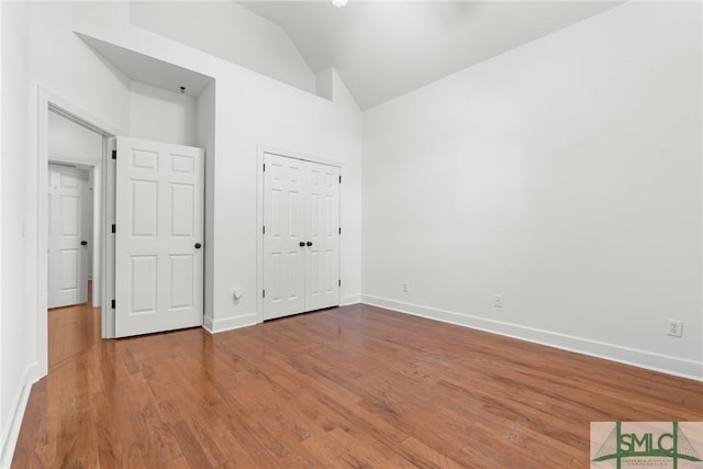 unfurnished bedroom featuring baseboards, high vaulted ceiling, and wood finished floors