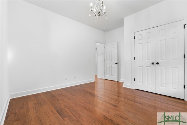 unfurnished bedroom featuring a closet, an inviting chandelier, baseboards, and wood finished floors