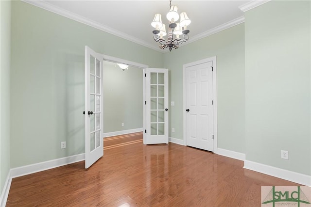 empty room with wood finished floors, baseboards, french doors, crown molding, and a notable chandelier