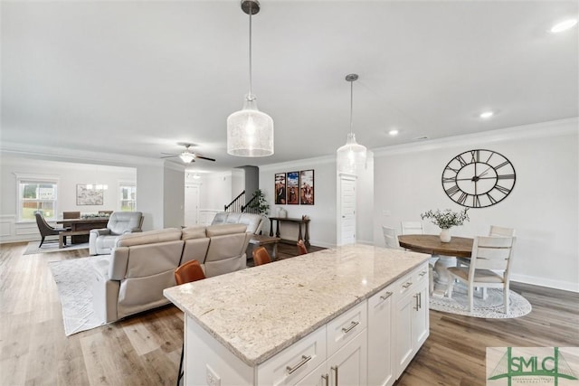 kitchen with a kitchen island, light stone counters, light hardwood / wood-style flooring, decorative light fixtures, and white cabinets