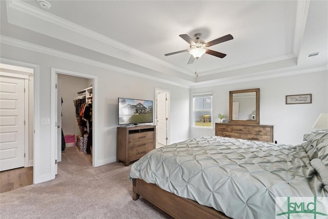 carpeted bedroom featuring a walk in closet, a tray ceiling, ceiling fan, and ornamental molding