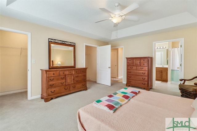 bedroom with ensuite bath, ceiling fan, a tray ceiling, a walk in closet, and a closet