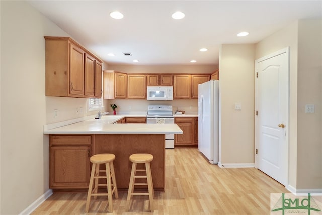 kitchen featuring a breakfast bar, white appliances, sink, light hardwood / wood-style floors, and kitchen peninsula