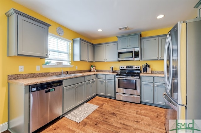 kitchen with gray cabinetry, sink, stainless steel appliances, and light hardwood / wood-style flooring