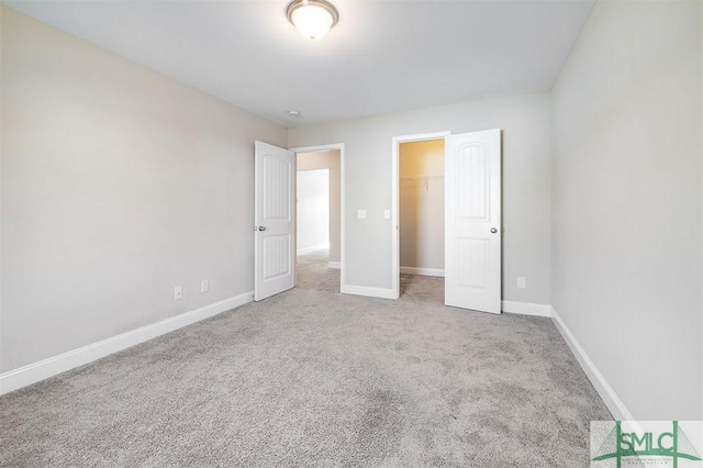 unfurnished bedroom with a walk in closet, baseboards, and carpet floors