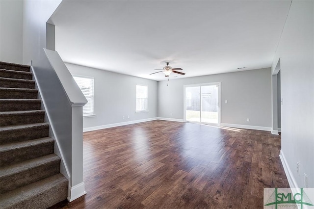 unfurnished living room with stairs, baseboards, ceiling fan, and dark wood-style flooring