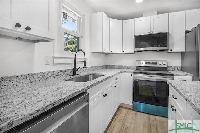 kitchen with light stone countertops, appliances with stainless steel finishes, sink, white cabinets, and light hardwood / wood-style floors