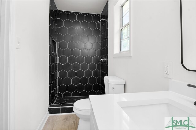 bathroom with a tile shower, hardwood / wood-style floors, vanity, and toilet