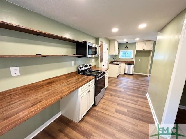 kitchen with white cabinets, wood counters, sink, and stainless steel appliances