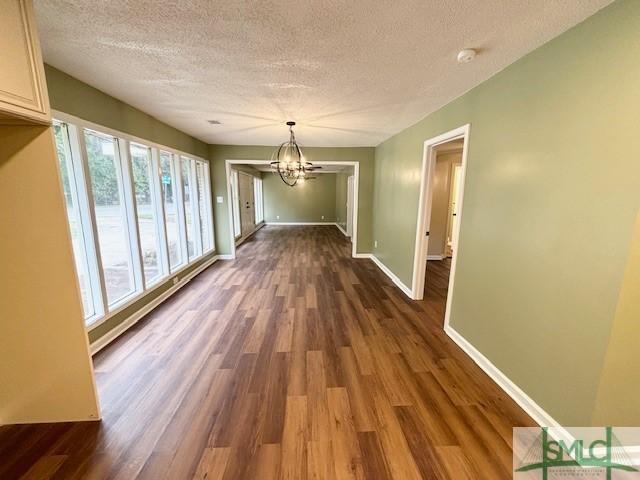 unfurnished dining area with a healthy amount of sunlight, dark wood-type flooring, a chandelier, and a textured ceiling