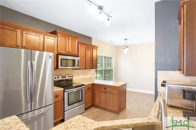 kitchen with tasteful backsplash, kitchen peninsula, pendant lighting, appliances with stainless steel finishes, and light wood-type flooring